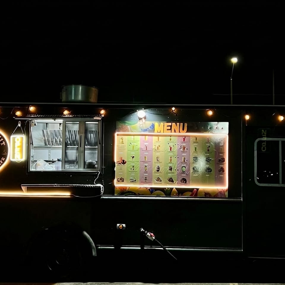 Illuminated black Real Fruta desserts and café food truck displaying its menu at night.